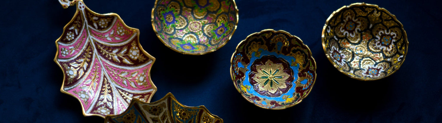 Enamelled brass leaf trays and painted bowls on navy velvet